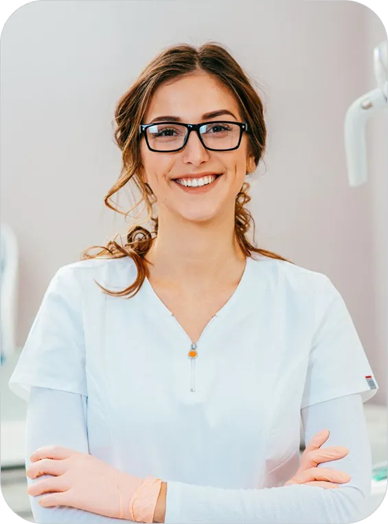 Smiling woman wearing glasses and a white medical uniform with arms crossed.