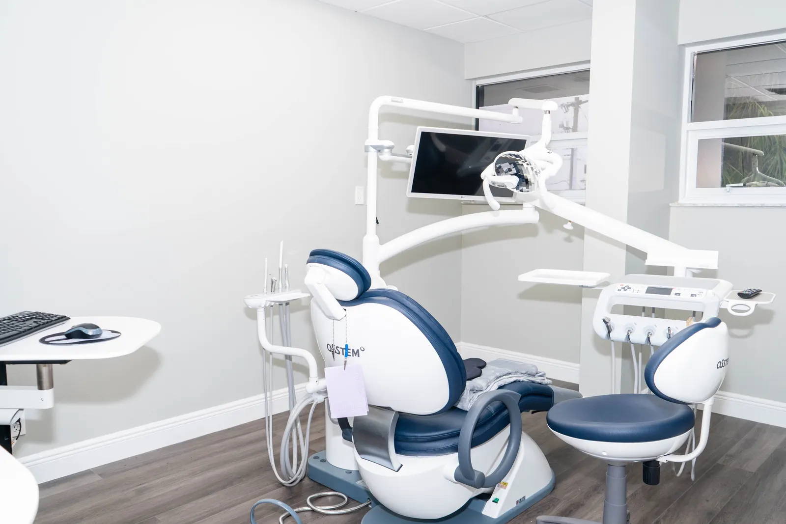 Modern dental office with blue and white dental chair, equipment, and a monitor on the wall.