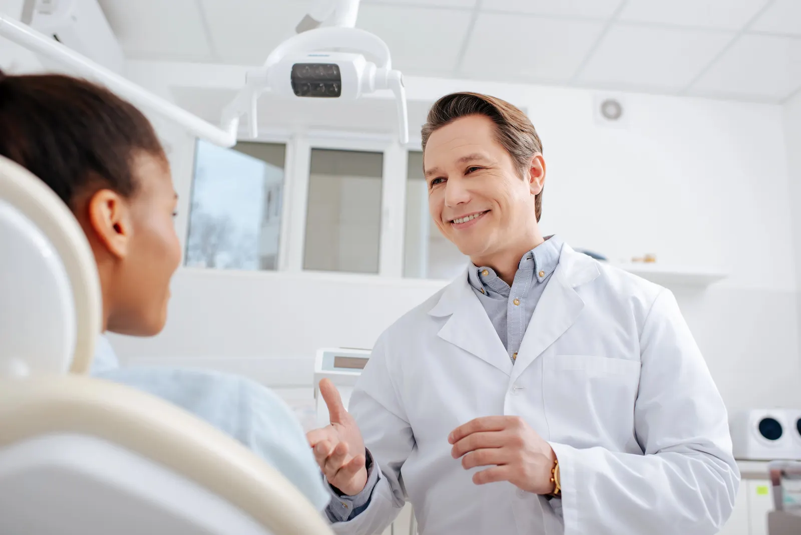 Smiling male dentist talking to female patient in a modern dental office.