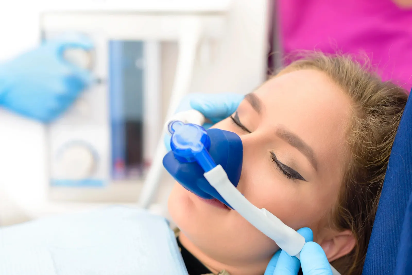 Close-up of a woman wearing a blue dental sedation mask with eyes closed during treatment.