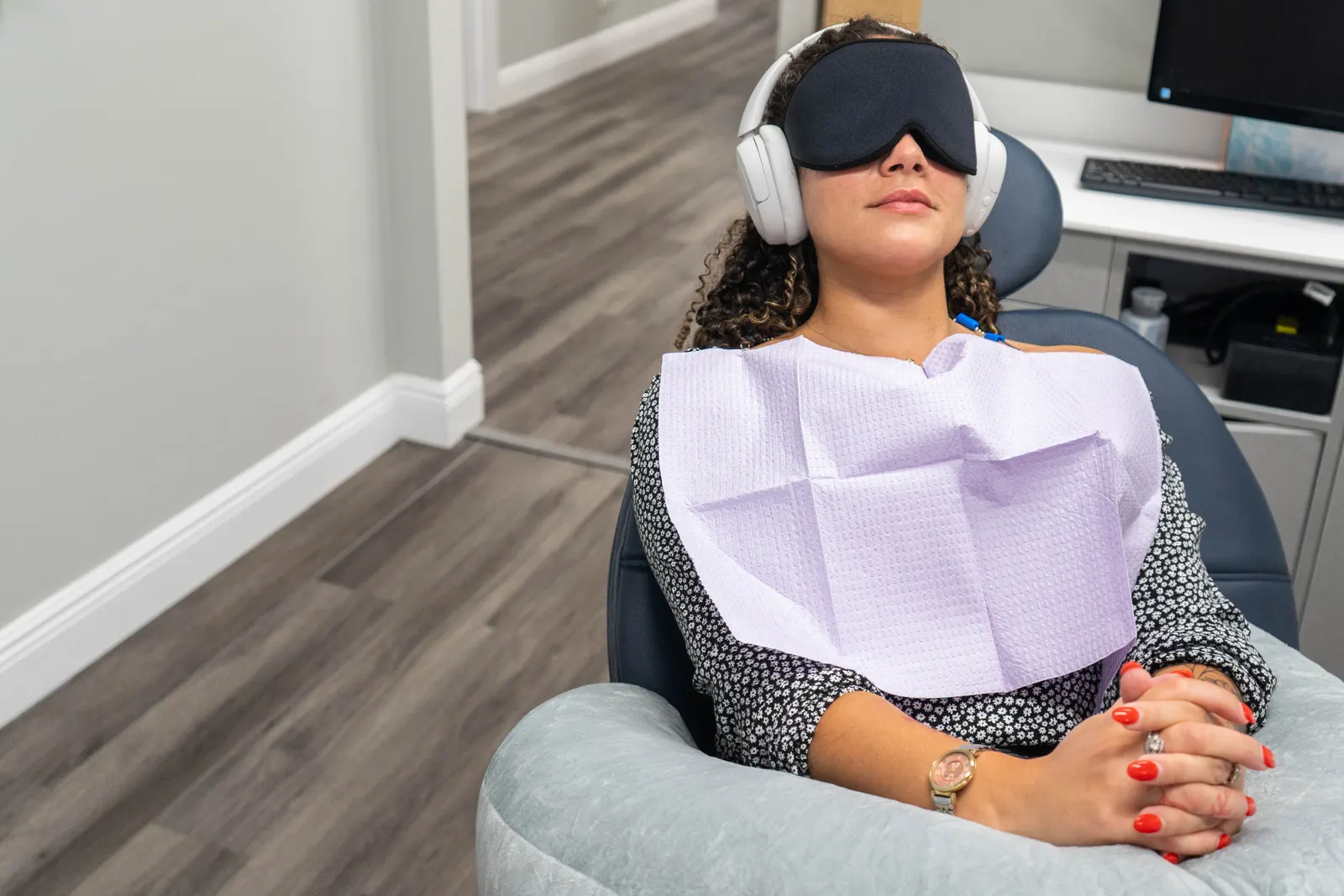 Woman reclining in dental chair wearing headphones and eye mask with a dental bib on.