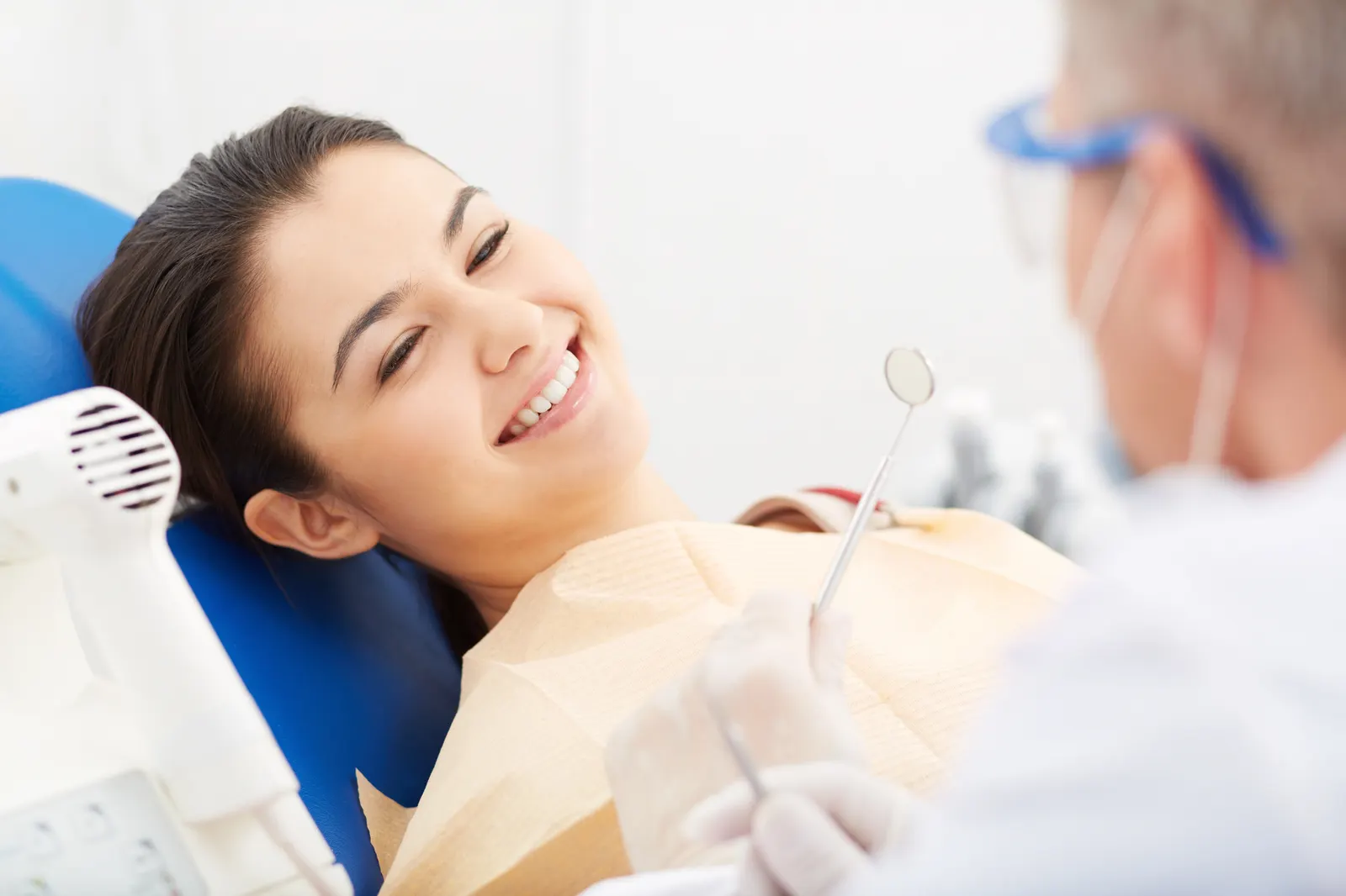 Smiling woman reclined in a dental chair with a dentist holding dental tools nearby.