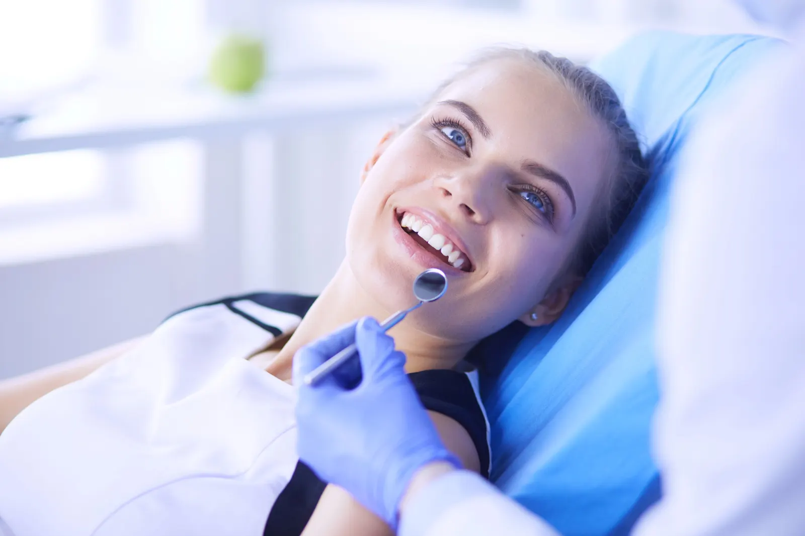 Smiling woman reclined in dental chair with dentist holding mirror near her teeth.