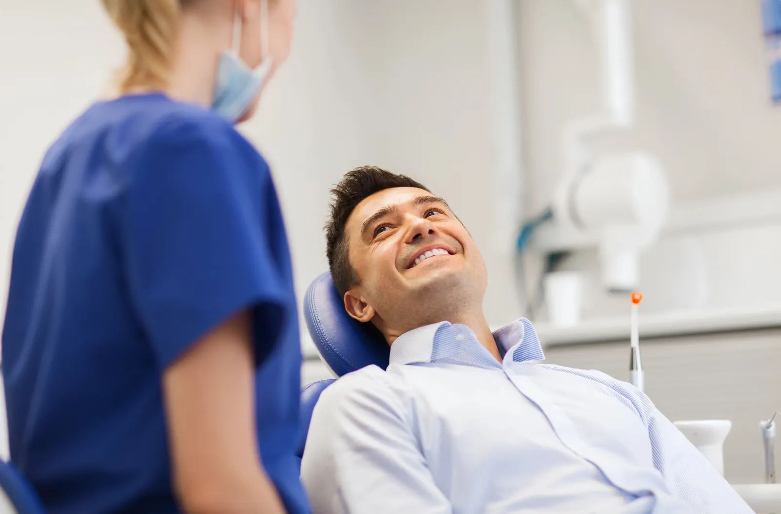 Smiling man in a dental chair looking at a female dentist wearing scrubs and a mask.