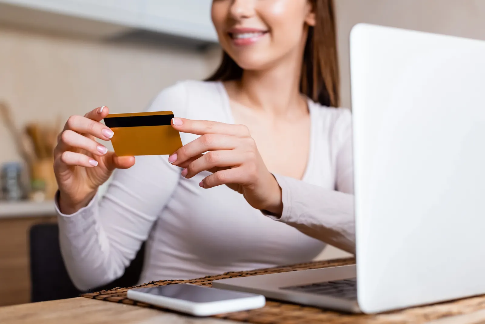 Woman holding a credit card near a laptop with a smartphone on the table.