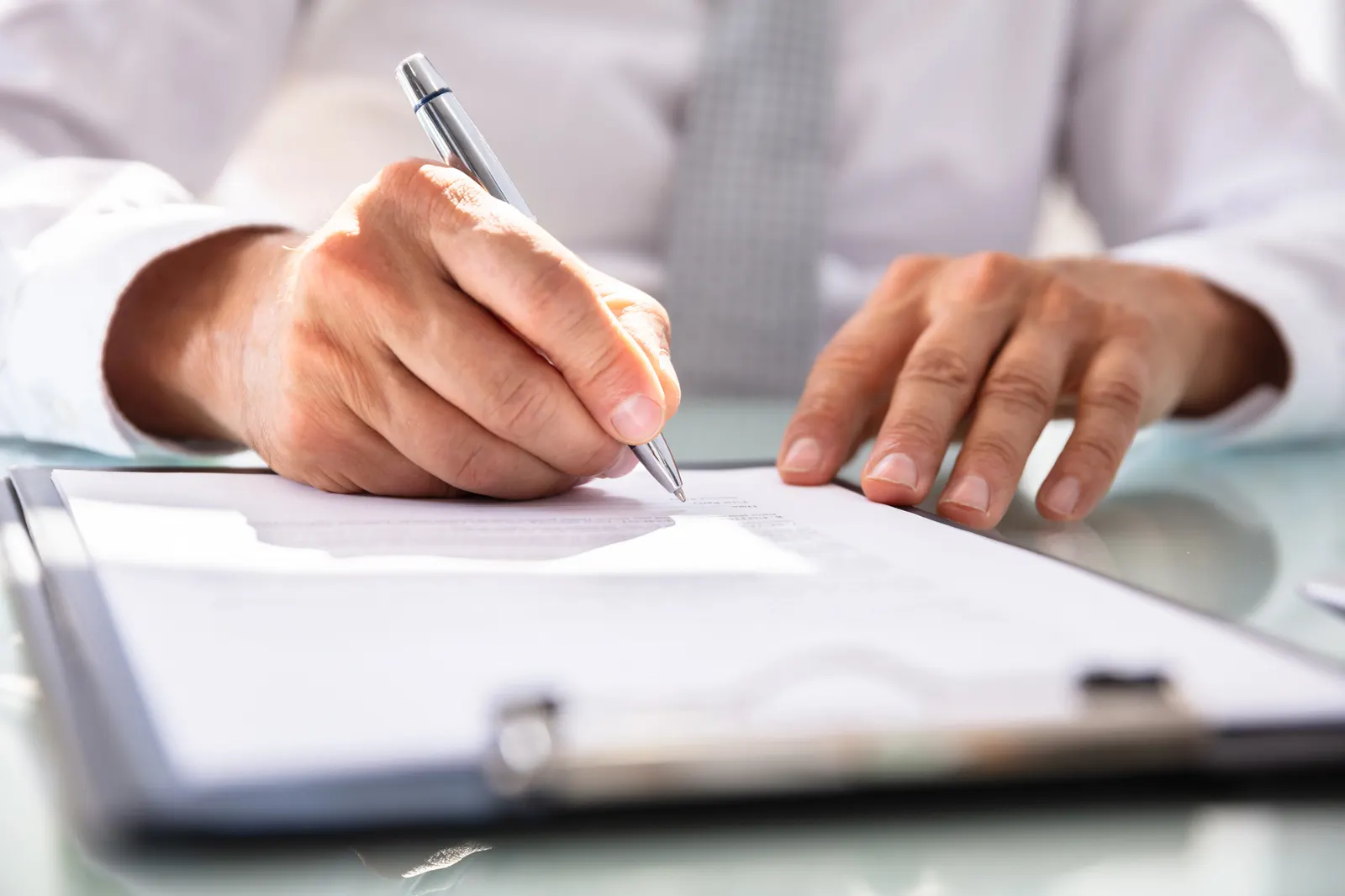 Person in business attire signing a document on a clipboard with a silver pen.