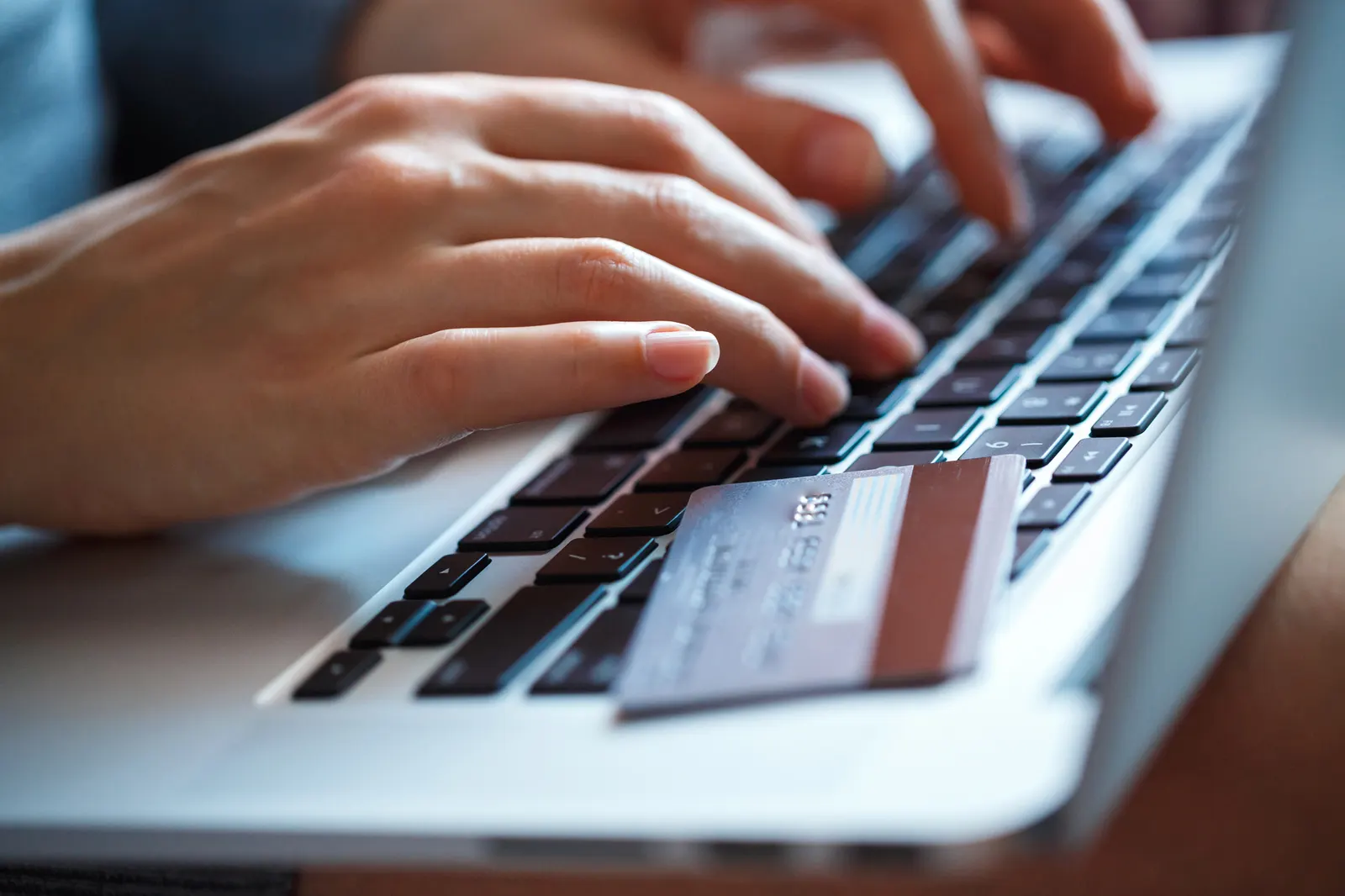 Hands typing on a laptop keyboard with a credit card resting on the keys.