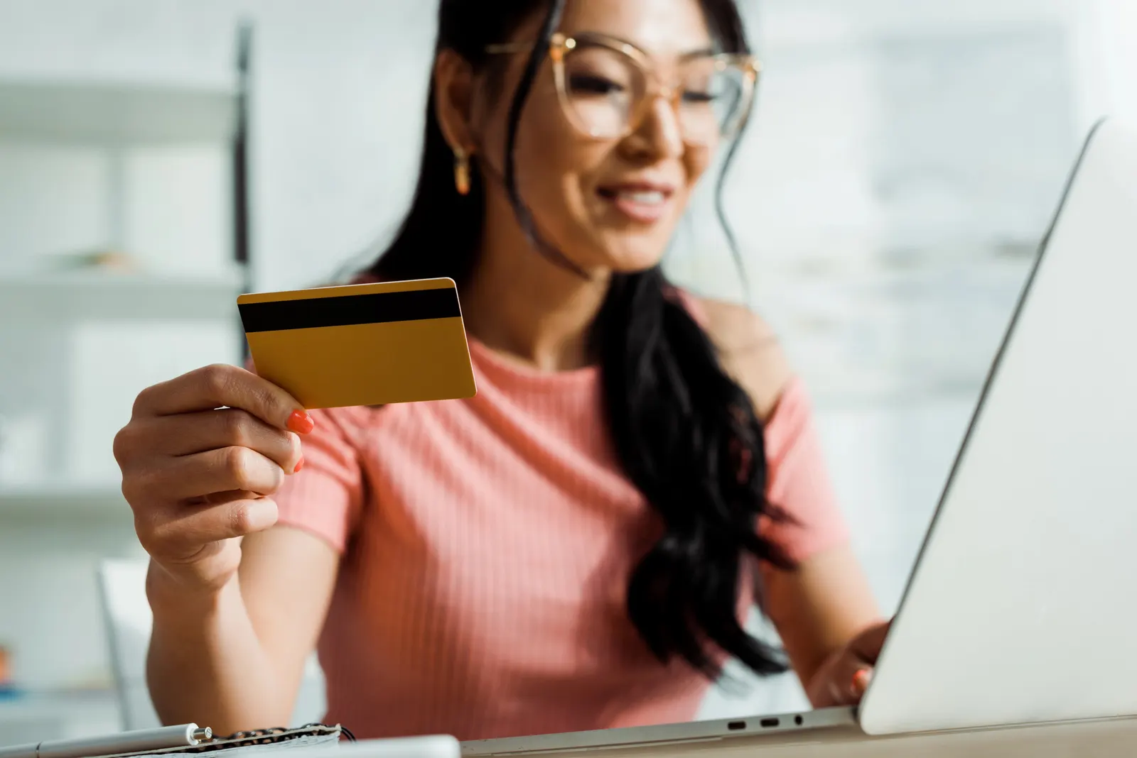 Woman holding a credit card and using a laptop, smiling in a bright room.