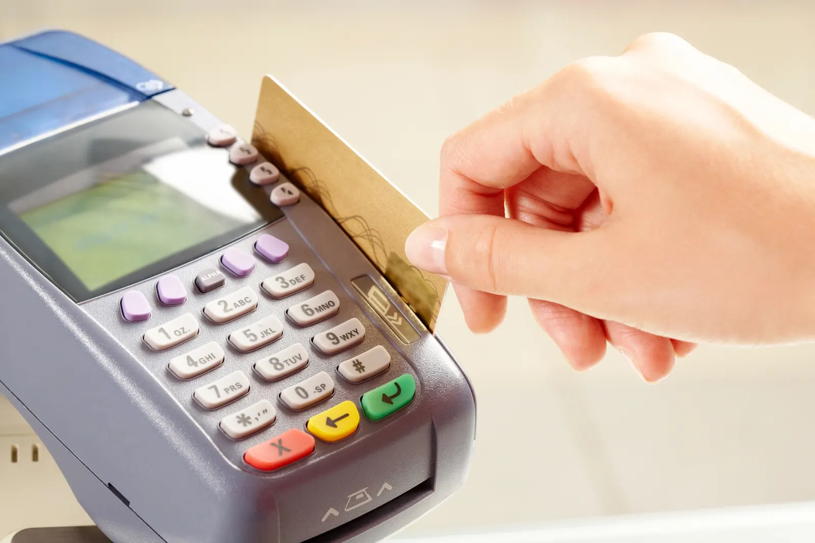 Hand inserting a gold credit card into a payment terminal with keypad and screen.