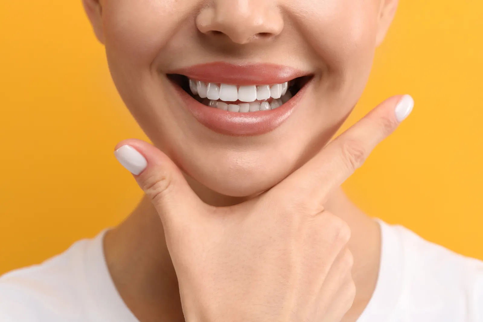 Close-up of a woman smiling with white nails holding her chin against an orange background.