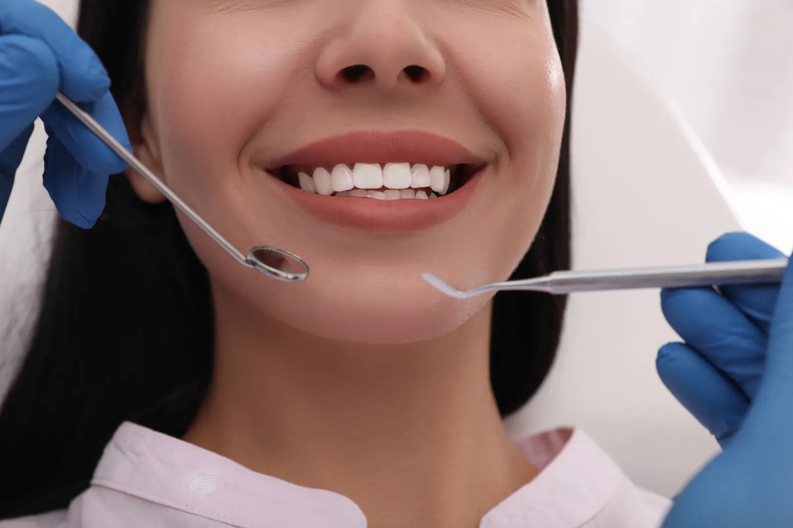 Close-up of a smiling woman’s mouth with dental tools near her teeth during a checkup.