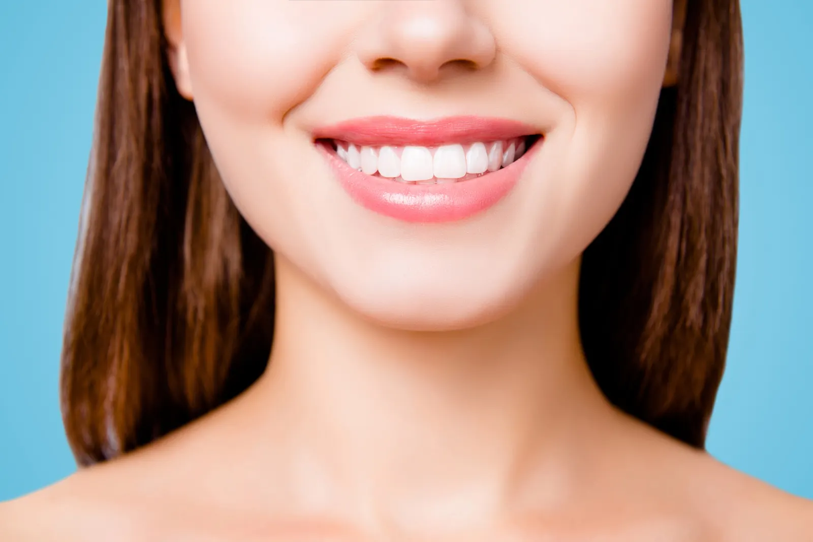 Close-up of a woman smiling with straight white teeth against a blue background.