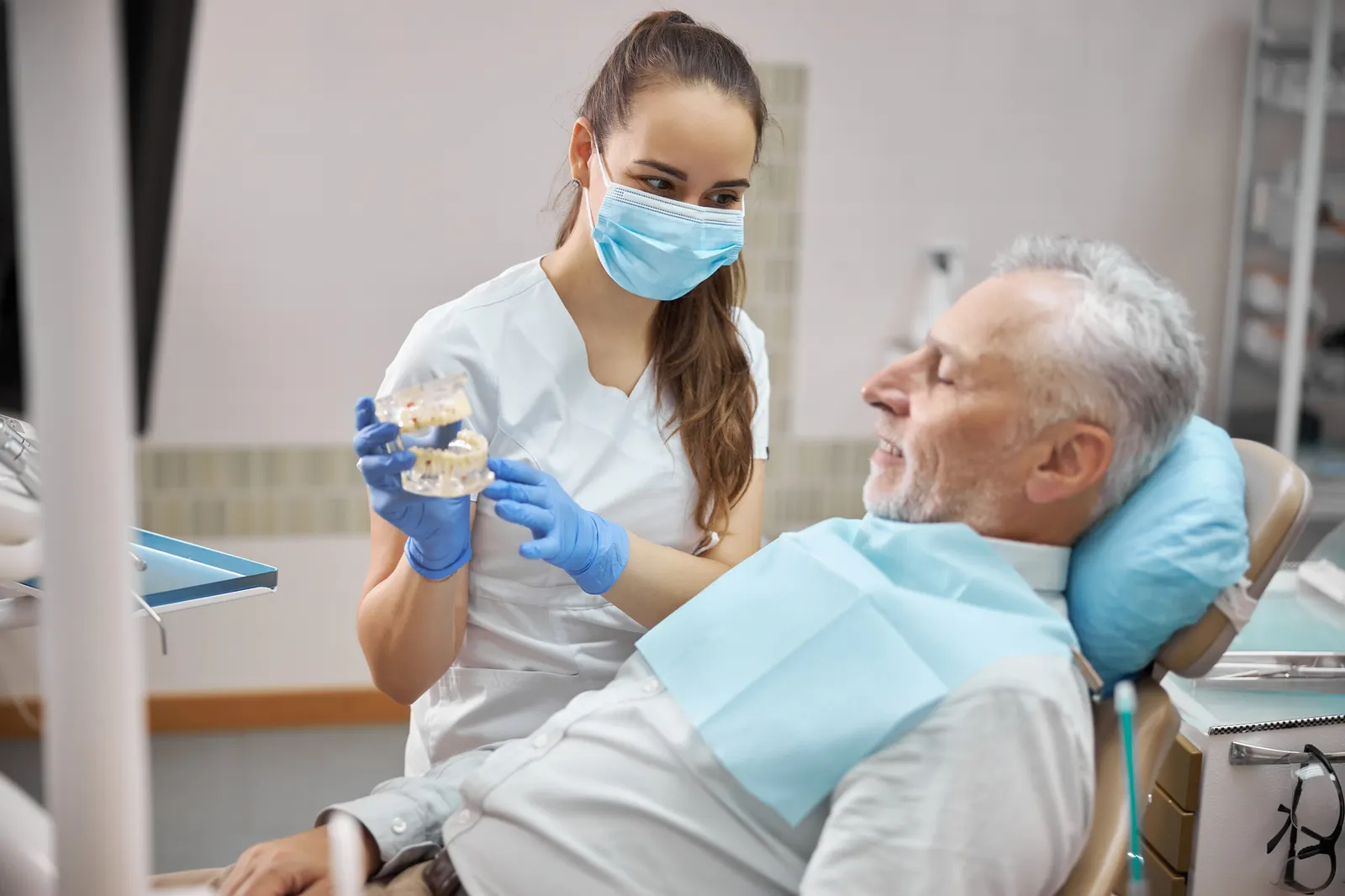 Dentist showing a dental model to a male patient reclining in a dental chair.