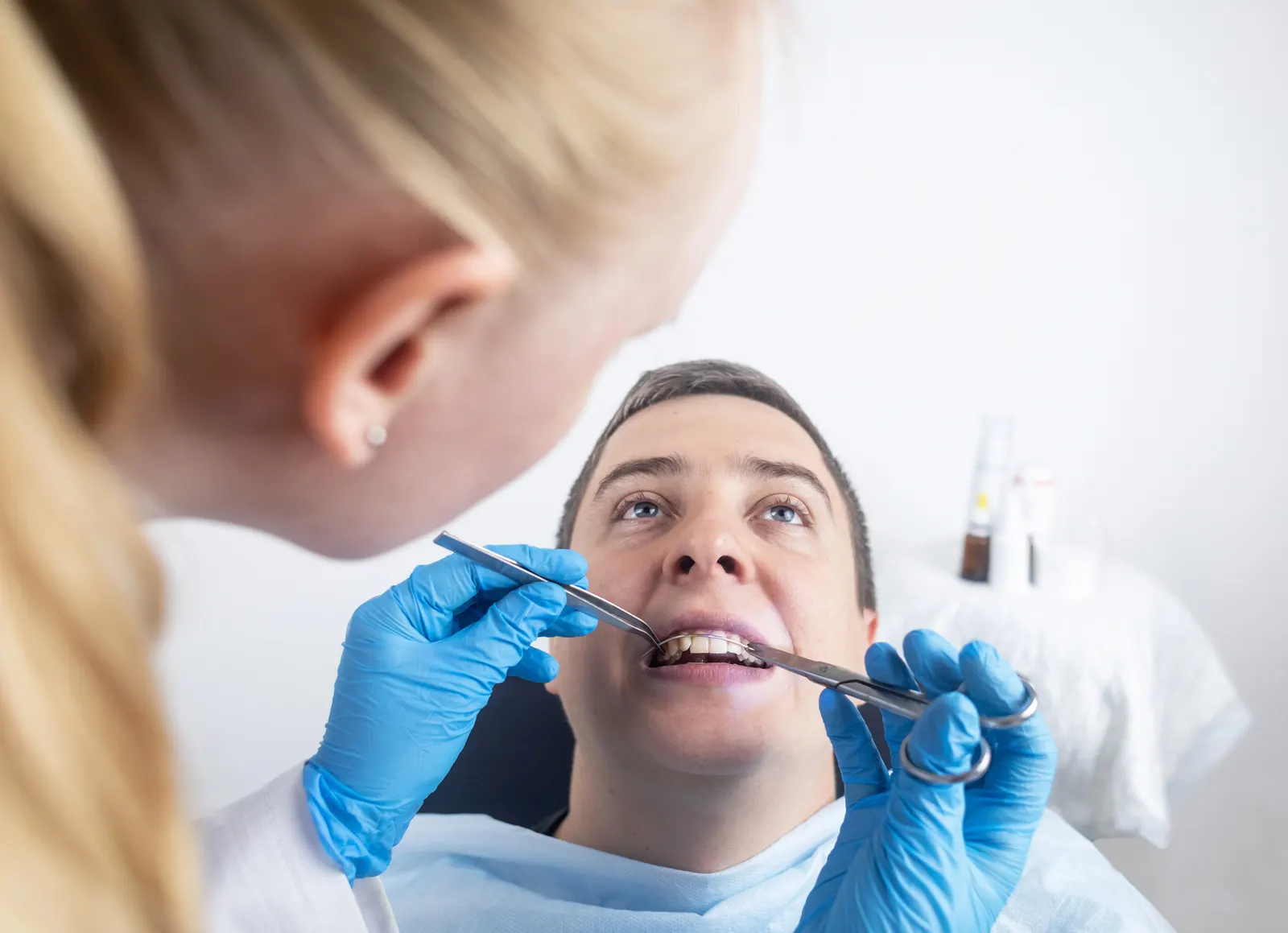 Dentist wearing blue gloves examining a male patient’s teeth with dental tools.