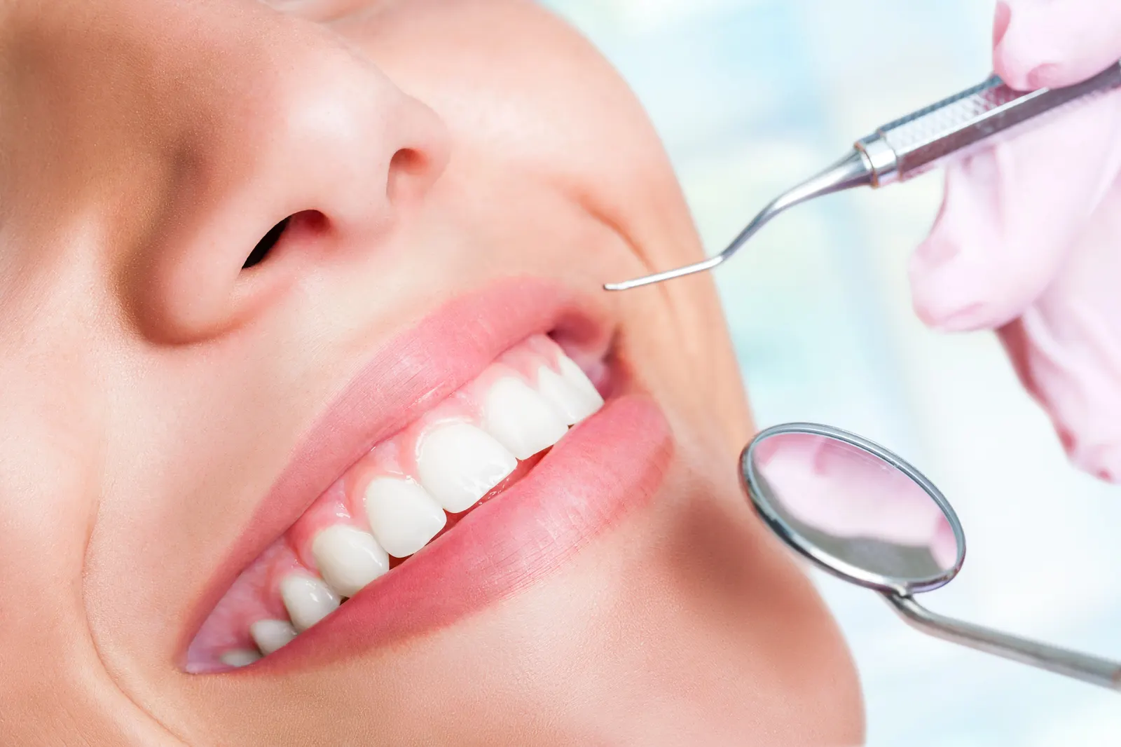 Close-up of a smiling person’s teeth with dental tools near the mouth during a checkup.