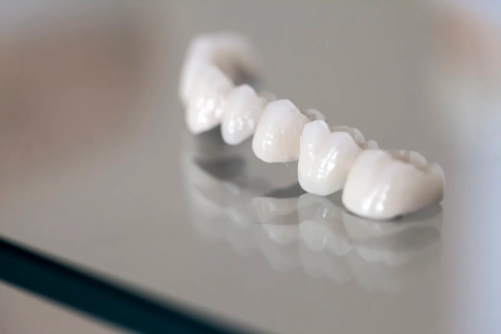 Close-up of dental crowns or veneers on a reflective surface, showing detailed tooth shapes.