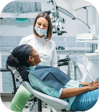 Dentist wearing a mask smiling at a patient reclining in a dental chair during consultation.